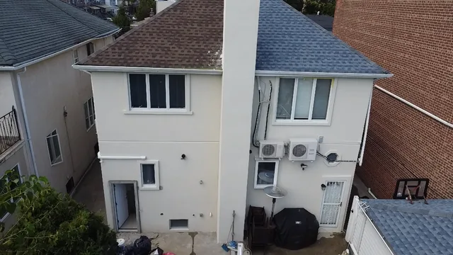 Rear exterior of a renovated two-story home with new white stucco, replacement windows, and a newly shingled roof.